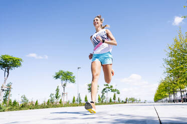 Mid erwachsene Frau joggen auf der Straße gegen blauen Himmel - JCMF01150