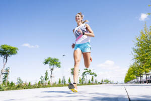 Mid erwachsene Frau joggen auf der Straße gegen blauen Himmel - JCMF01150