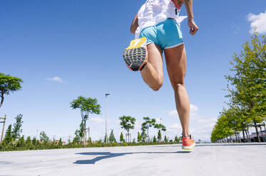 Beine einer mittleren erwachsenen Frau, die auf der Straße gegen den blauen Himmel an einem sonnigen Tag läuft - JCMF01151