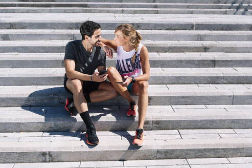 Smiling couple looking at each other while sitting on steps in city during sunny day - JCMF01153