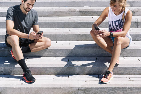 Ein Paar benutzt sein Smartphone auf einer Treppe in der Stadt an einem sonnigen Tag - JCMF01154