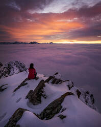 Frau bewundert stimmungsvollen Sonnenuntergang vom schneebedeckten Gipfel des Aggenstein - MALF00028