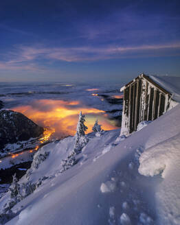 Hütte in schneebedeckten Bergen bei Nacht mit Lichtern in der Ferne - MALF00039