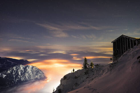 Abgeschiedene Berghütte in der Abenddämmerung mit beleuchtetem Tal im Hintergrund - MALF00050
