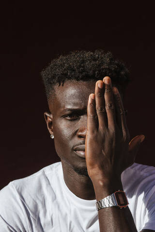 Nahaufnahme eines afrikanischen jungen Mannes, der sein Gesicht mit der Hand bedeckt, lizenzfreies Stockfoto