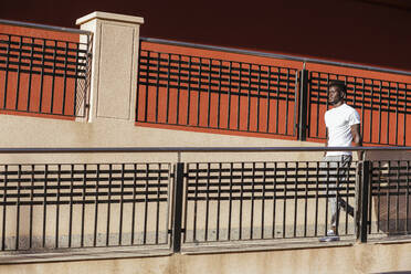 Young man walking on footpath in city during sunny day - LJF01698