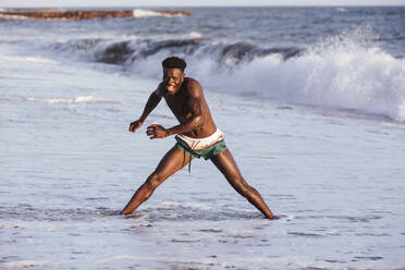 Shirtless cheerful young man exercising while standing in sea - LJF01704