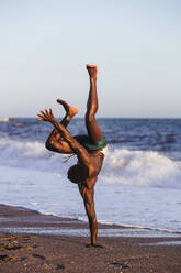 Shirtless young man doing handstand at beach against clear sky - LJF01710