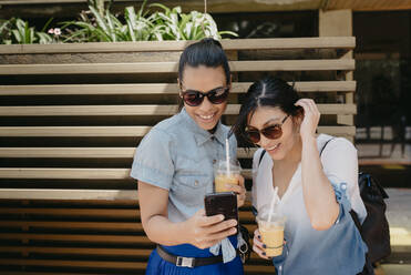 Freundinnen mit Sonnenbrille, die ein Foto über ein Smartphone in der Stadt betrachten - DSIF00069