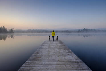 Woman standing at edge of lakeshore jetty at foggy dawn - LBF03176