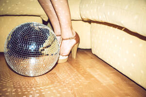 Junge Frau mit hohen Absätzen, die auf einer Party neben einer Discokugel auf dem Boden steht - EHF00694