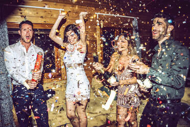 Happy friends opening champagne while dancing amidst confetti in party - EHF00695