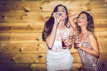 Drunk female friends with props and drinks standing against wall in party - EHF00698