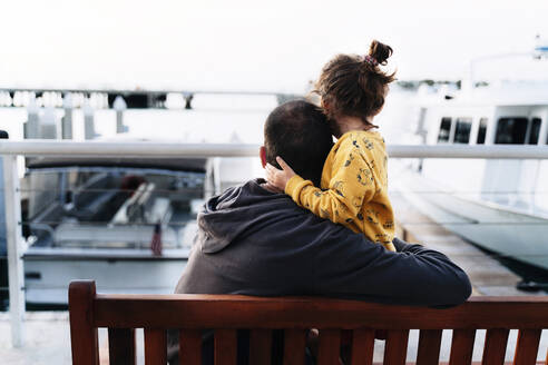 Liebevoller Vater, der seine Tochter umarmt, während er auf das Meer in der Stadt blickt - GEMF03947