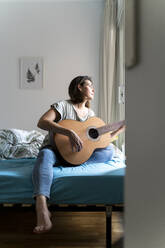 Woman playing guitar in bedroom - AFVF06873