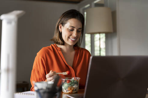 Smiling business person eating salad at home - AFVF06880