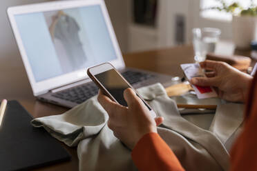 Ausgeschnittenes Bild einer Geschäftsfrau mit Kreditkarte und Telefon, die zu Hause Kleidung online zurückgibt - AFVF06890