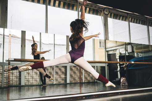 Rückenansicht einer jungen, schlanken Ballerina, die im Studio über den Boden springt und die Beine bewegt. - ADSF07190