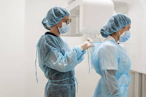 Female doctor tying nurse's protective wear at clinic - DLTSF00963