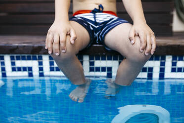 Junge sitzt mit den Händen auf den Knien am Pool - JRFF04675