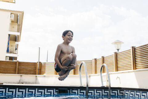 Aufgeregter Junge springt im Pool gegen den Himmel im Sommer, lizenzfreies Stockfoto