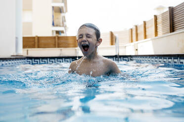 Happy boy enjoying in swimming pool during summer - JRFF04680