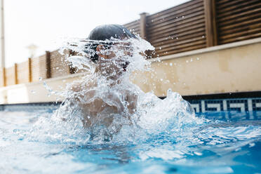 Boy splashing water around face in pool during summer - JRFF04682