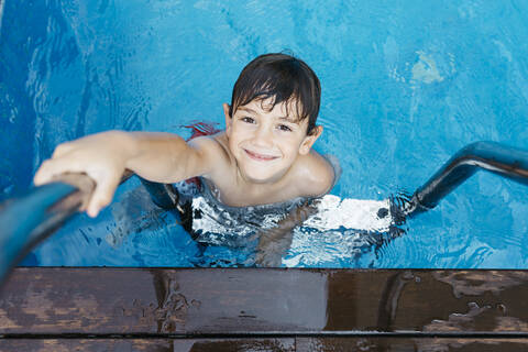 Smiling boy holding ladder while standing in swimming Pool stock photo