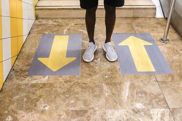 Beine eines jungen Mannes, der neben Pfeilsymbolen auf dem Boden einer U-Bahn-Station steht - EGAF00601