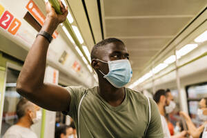 Young man wearing mask looking away while standing in subway train - EGAF00609