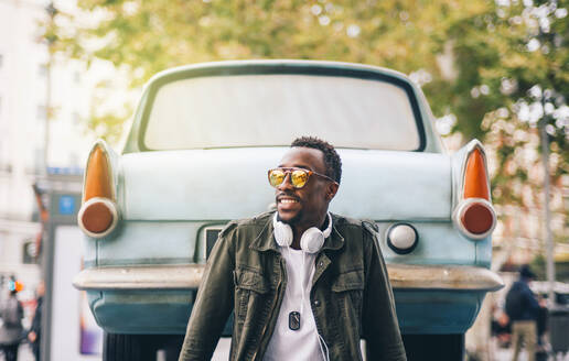 Junger Mann mit Sonnenbrille sitzt an einem Oldtimer in der Stadt - OCMF01579