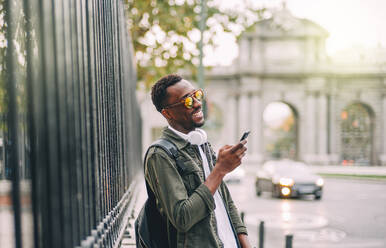 Lächelnder Mann mit Sonnenbrille, der ein Smartphone benutzt, während er in der Stadt steht - OCMF01581