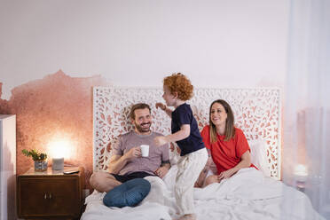 Parents looking at playful son while relaxing on bed - EIF00143