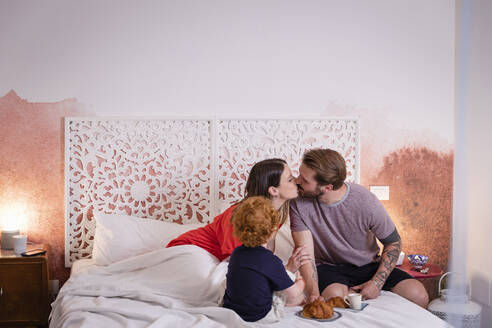 Eltern küssen sich beim Frühstück mit dem Sohn im Bett zu Hause - EIF00145