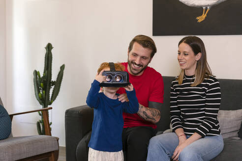 Lächelnde Eltern, die ihren Sohn in einem Virtual-Reality-Simulator im Wohnzimmer beobachten - EIF00159