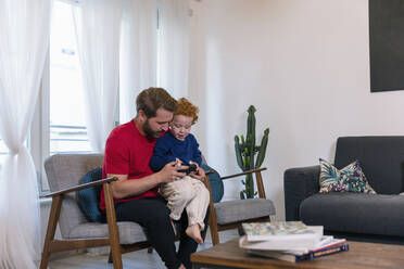 Father with cute son holding joystick while playing video game in living room at home - EIF00161