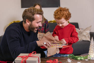 Cute son with father opening Christmas present in living room at home - EIF00169
