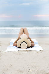 Schwangere Frau mit Bikini und Sonnenhut am Strand liegend - CAVF87701