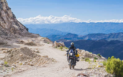Mann auf Tourenmotorrad auf Schotterstraße in Bolivien - CAVF87745