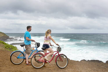 Pärchen auf Fahrrädern mit Blick auf den Ozean an der Küste von Kauai, in der Nähe von Kapaa, Kauai, Hawaii, Vereinigte Staaten von Amerika, Nordamerika - RHPLF17137