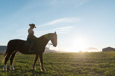 Frau reitet Pferd gegen Sonnenuntergang Himmel auf Ranch - ADSF07300