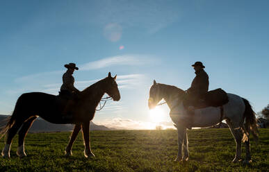 Mann und Frau reiten auf Pferden gegen den Sonnenuntergang auf einer Ranch - ADSF07302