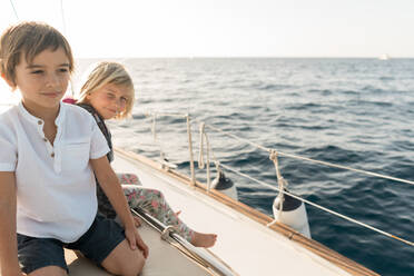 Seitenansicht der positiven Kinder sitzen auf Seitendeck des teuren Boot schwimmt auf dem Wasser in sonnigen Tag - ADSF07311