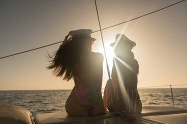 Rückenansicht von schönen jungen Frauen in Sonnenbrillen und Kapitän Hüte sitzen auf Deck des teuren Boot schwimmt auf dem Wasser bei Sonnenuntergang - ADSF07312