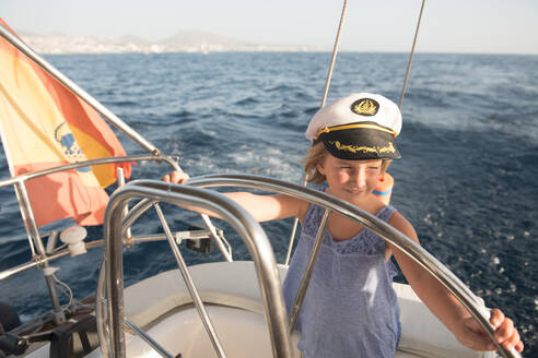 Positive Kind in Kapitän Hut schwimmend auf teuren Boot auf dem Meer in sonnigen Tag - ADSF07313