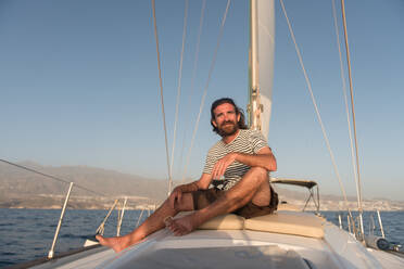 Positive bearded adult male in sunglasses sitting floating on expensive boat on sea in sunny day - ADSF07321