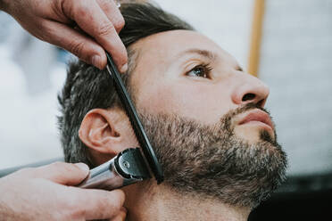 Closeup Ernte Hände der Barbier mit Kamm und Trimmer Schneiden Bart der männlichen sitzen in Barbershop auf unscharfen Hintergrund - ADSF07332