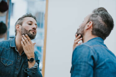 Reflection in mirror of handsome stylish male checking beard in salon - ADSF07335