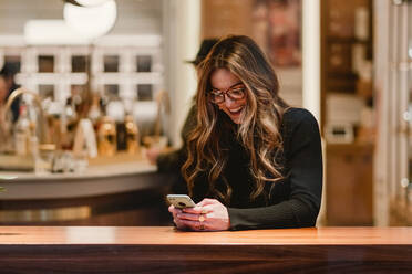 Fröhliche Frau mit Smartphone in einem Café - ADSF07386