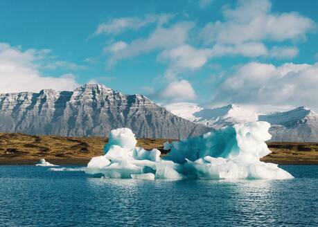Malerischer Blick auf Eis auf der Wasseroberfläche im Winter und blauer Himmel mit Wolken in Island in der Nähe von Bergen und Küstenlinie - ADSF07407
